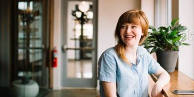 A happy woman sitting at a narrow desk looking to someone off-frame.
