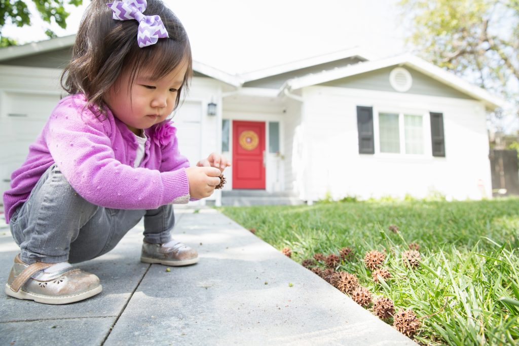 An asian female toddler squatted on the pavement in front of her family home.