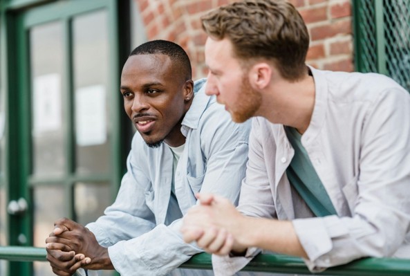 Two men leaning over a green railing, talking.