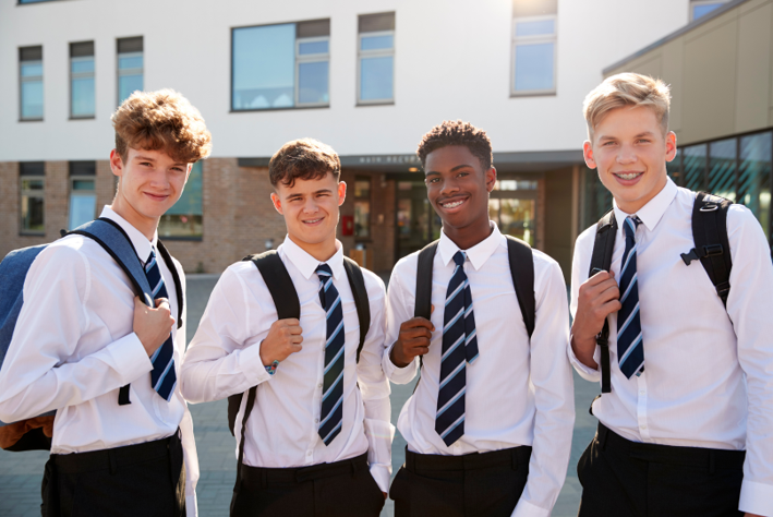 Four boys in uniform, standing outside secondary school, grinning.